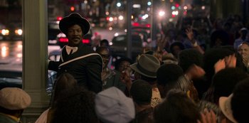 Movie still from “Dolemite Is My Name” (2019), directed by Craig Brewer – A group of people gathered in the street at night; Medium shot, Over the shoulder angle