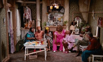 Movie still from “Don't Play Us Cheap” (1972), directed by Melvin Van Peebles – A group of people sitting around a living room together; Wide shot, High angle