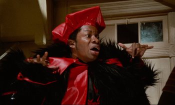 Movie still from “Don't Play Us Cheap” (1972), directed by Melvin Van Peebles – A man wearing a red and black hat and a black jacket; Close Up shot, Low angle