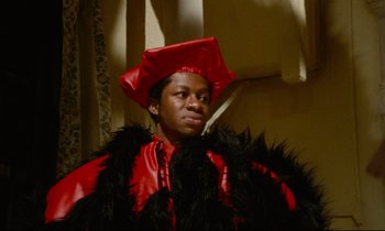 Movie still from “Don't Play Us Cheap” (1972), directed by Melvin Van Peebles – A man in a red and black costume; Medium shot, Low angle