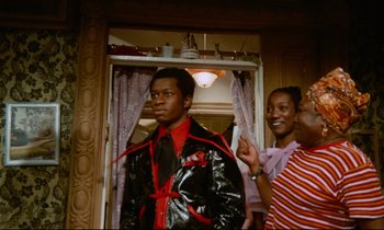 Movie still from “Don't Play Us Cheap” (1972), directed by Melvin Van Peebles – A man in a black and red jacket and a woman in a pink shirt; Medium shot, Over the shoulder angle