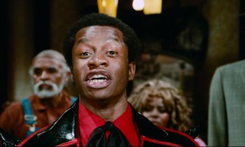 Movie still from “Don't Play Us Cheap” (1972), directed by Melvin Van Peebles – A man in a red and black shirt and black tie; Close Up shot, Low angle