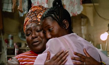 Movie still from “Don't Play Us Cheap” (1972), directed by Melvin Van Peebles – Two women are hugging each other in front of a window; Close Up shot, High angle