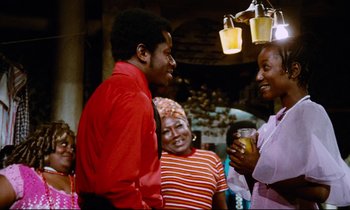 Movie still from “Don't Play Us Cheap” (1972), directed by Melvin Van Peebles – A group of people standing next to each other in a room; Medium shot, Over the shoulder angle