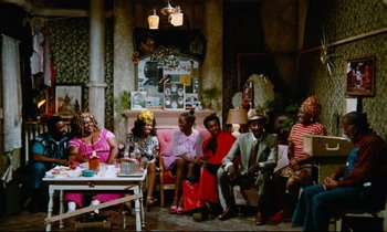 Movie still from “Don't Play Us Cheap” (1972), directed by Melvin Van Peebles – A group of people sitting around a living room together; Wide shot, High angle