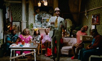 Movie still from “Don't Play Us Cheap” (1972), directed by Melvin Van Peebles – A group of people sitting in a living room; Wide shot, High angle