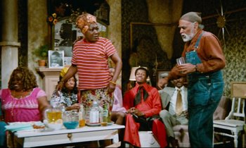 Movie still from “Don't Play Us Cheap” (1972), directed by Melvin Van Peebles – A group of people sitting around a table with drinks on it; Wide shot, High angle