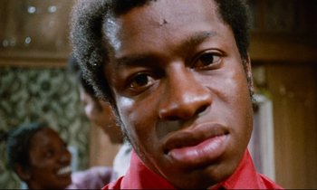 Movie still from “Don't Play Us Cheap” (1972), directed by Melvin Van Peebles – A person wearing a red shirt; Close Up shot, Low angle