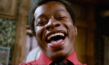 Movie still from “Don't Play Us Cheap” (1972), directed by Melvin Van Peebles – A person laughing with his mouth open; Close Up shot, Low angle