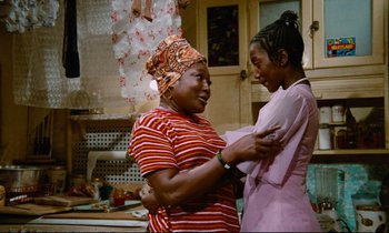 Movie still from “Don't Play Us Cheap” (1972), directed by Melvin Van Peebles – Two women are hugging in the kitchen; Medium shot, Low angle