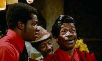 Movie still from “Don't Play Us Cheap” (1972), directed by Melvin Van Peebles – A group of men standing next to each other in a room; Close Up shot, Low angle
