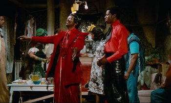 Movie still from “Don't Play Us Cheap” (1972), directed by Melvin Van Peebles – A group of people standing in a room; Wide shot, Low angle