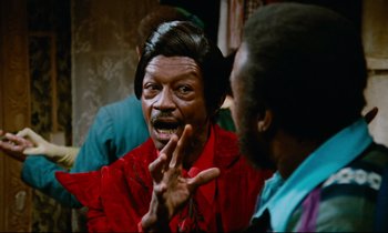 Movie still from “Don't Play Us Cheap” (1972), directed by Melvin Van Peebles – A man in a red shirt is talking to another man in a red shirt; Close Up shot, Over the shoulder angle