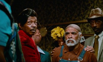 Movie still from “Don't Play Us Cheap” (1972), directed by Melvin Van Peebles – A group of men standing next to each other; Medium shot, Over the shoulder angle