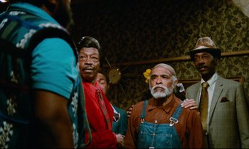 Movie still from “Don't Play Us Cheap” (1972), directed by Melvin Van Peebles – A group of men standing next to each other in a room; Medium shot, Low angle