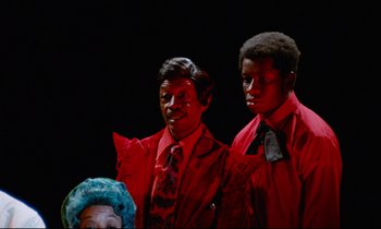 Movie still from “Don't Play Us Cheap” (1972), directed by Melvin Van Peebles – A couple of men standing next to each other on top of a stage; Medium shot, High angle