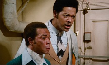 Movie still from “Don't Play Us Cheap” (1972), directed by Melvin Van Peebles – A couple of men standing next to each other; Medium shot, Low angle