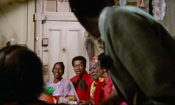 Movie still from “Don't Play Us Cheap” (1972), directed by Melvin Van Peebles – A group of people sitting around a table; Medium shot, Over the shoulder angle