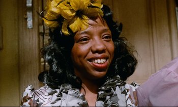 Movie still from “Don't Play Us Cheap” (1972), directed by Melvin Van Peebles – A person wearing a flower in her hair; Close Up shot, Low angle
