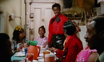 Movie still from “Don't Play Us Cheap” (1972), directed by Melvin Van Peebles – A group of people sitting at a table with food; Medium shot, Over the shoulder angle