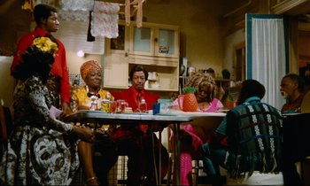 Movie still from “Don't Play Us Cheap” (1972), directed by Melvin Van Peebles – A group of people sitting around a table; Wide shot, Low angle