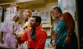 Movie still from “Don't Play Us Cheap” (1972), directed by Melvin Van Peebles – A group of people standing in a room; Medium shot, Low angle