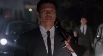 Movie still from “Double Impact” (1991), directed by Sheldon Lettich – A man in a suit and tie holding a gun; Close Up shot, Low angle