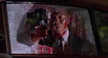 Movie still from “Double Impact” (1991), directed by Sheldon Lettich – A man with blood on his face holding a gun in front of a window; Close Up shot, Low angle