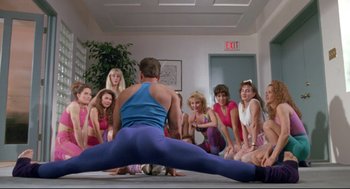 Movie still from “Double Impact” (1991), directed by Sheldon Lettich – A group of people sitting and standing around a man doing a split; Wide shot, Low angle