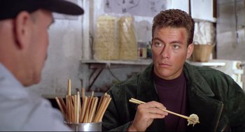 Movie still from “Double Impact” (1991), directed by Sheldon Lettich – A man holding chopsticks in front of a bunch of chopsticks; Close Up shot, Over the shoulder angle