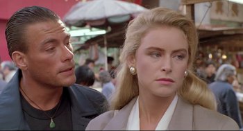 Movie still from “Double Impact” (1991), directed by Sheldon Lettich – A man and a woman standing next to each other in front of an umbrella; Close Up shot, Over the shoulder angle