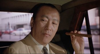 Movie still from “Double Impact” (1991), directed by Sheldon Lettich – A man sitting in the back of a car smoking a cigar; Close Up shot, Low angle