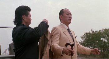 Movie still from “Double Impact” (1991), directed by Sheldon Lettich – A man in a suit and tie holding onto a jacket; Medium shot, Low angle