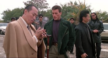 Movie still from “Double Impact” (1991), directed by Sheldon Lettich – A group of men standing next to each other on a field; Medium shot, Over the shoulder angle