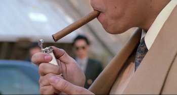 Movie still from “Double Impact” (1991), directed by Sheldon Lettich – A man smoking a cigar while holding a lighter in his mouth; Extreme Close Up shot, Low angle