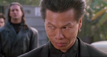 Movie still from “Double Impact” (1991), directed by Sheldon Lettich – A person wearing a suit and tie; Close Up shot, Low angle