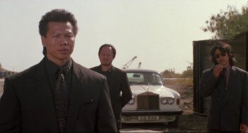 Movie still from “Double Impact” (1991), directed by Sheldon Lettich – Two men in suits standing in front of a car; Medium shot, Low angle