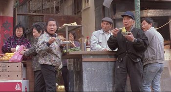 Movie still from “Double Impact” (1991), directed by Sheldon Lettich – A group of people standing around eating food; Wide shot, High angle