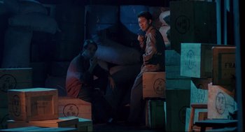 Movie still from “Double Impact” (1991), directed by Sheldon Lettich – Two men sitting next to each other on boxes; Medium shot, High angle