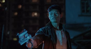 Movie still from “Double Impact” (1991), directed by Sheldon Lettich – A young man holding a gun in a dark city setting; Medium shot, Low angle