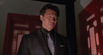 Movie still from “Double Impact” (1991), directed by Sheldon Lettich – A man wearing a suit and tie standing in a room; Close Up shot, Low angle
