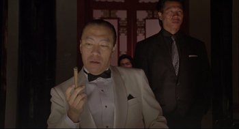 Movie still from “Double Impact” (1991), directed by Sheldon Lettich – A man in a white suit holding a cigarette in his hand; Medium shot, Low angle