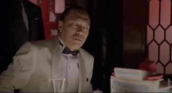 Movie still from “Double Impact” (1991), directed by Sheldon Lettich – A man wearing a suit and bow tie looking at the camera; Close Up shot, Low angle