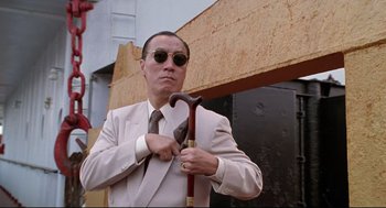 Movie still from “Double Impact” (1991), directed by Sheldon Lettich – A man in a suit and sunglasses holding a cane; Medium shot, Low angle