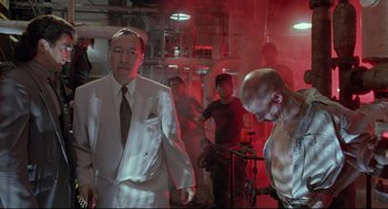 Movie still from “Double Impact” (1991), directed by Sheldon Lettich – A group of men standing around in a room; Medium shot, Low angle