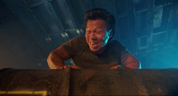 Movie still from “Double Impact” (1991), directed by Sheldon Lettich – An asian man is laughing while leaning on a wall; Medium shot, Low angle