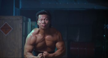 Movie still from “Double Impact” (1991), directed by Sheldon Lettich – A man with no shirt is posing for a picture; Medium shot, Low angle