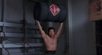 Movie still from “Double Impact” (1991), directed by Sheldon Lettich – A shirtless man holding a barrel above his head; Medium shot, Low angle