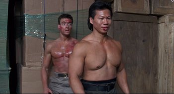 Movie still from “Double Impact” (1991), directed by Sheldon Lettich – Two shirtless men standing next to each other in a room; Medium shot, Low angle