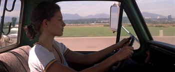 Movie still from “Double Jeopardy” (1999), directed by Bruce Beresford – A woman sitting in the driver's seat of a car driving down a road; Medium shot, Over the shoulder angle